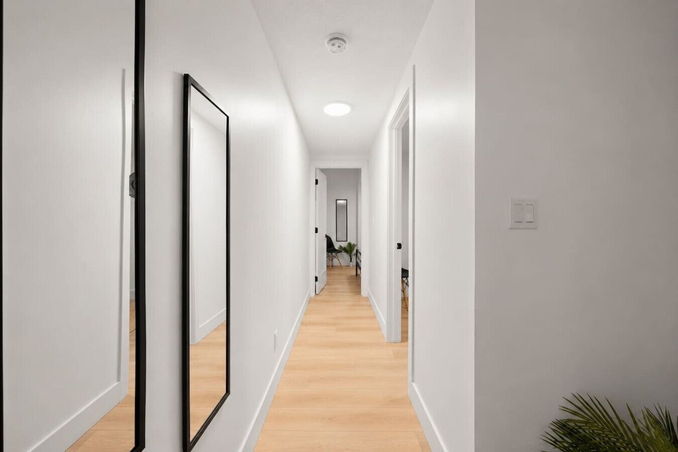 A hallway with white walls and wooden flooring, leading to a room with a door at the end.