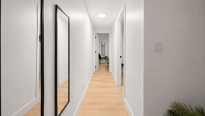 Un pasillo con paredes blancas y piso de madera, que conduce a una habitación con una puerta al final.