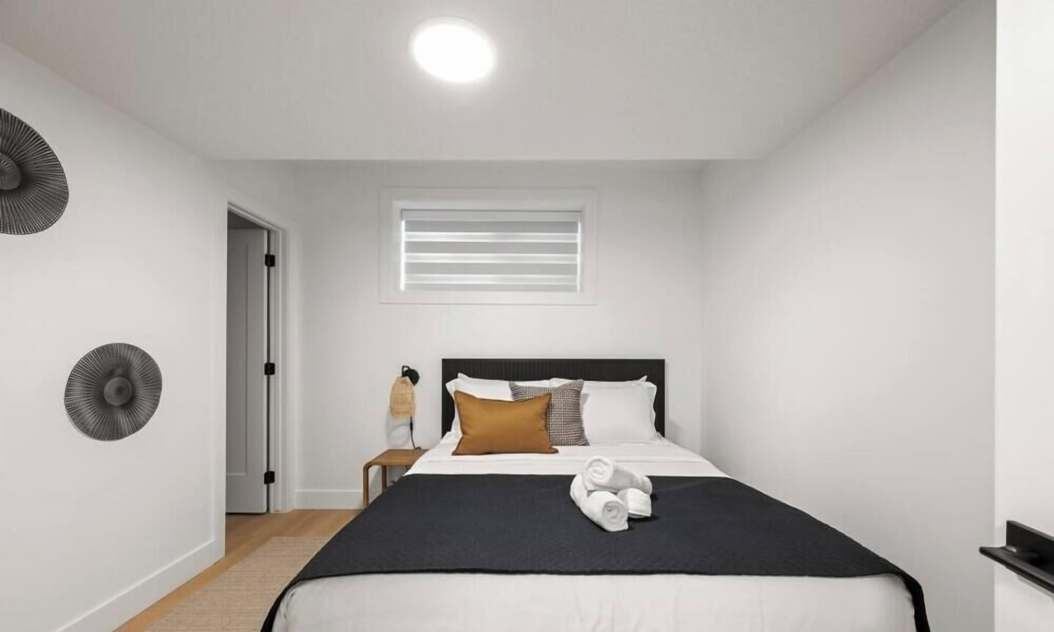 A modern bedroom with a bed, a window with blinds, a wall-mounted fan, and a door.