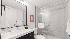 Un baño moderno con cabina de ducha de vidrio, lavamanos blanco y tocador negro.
