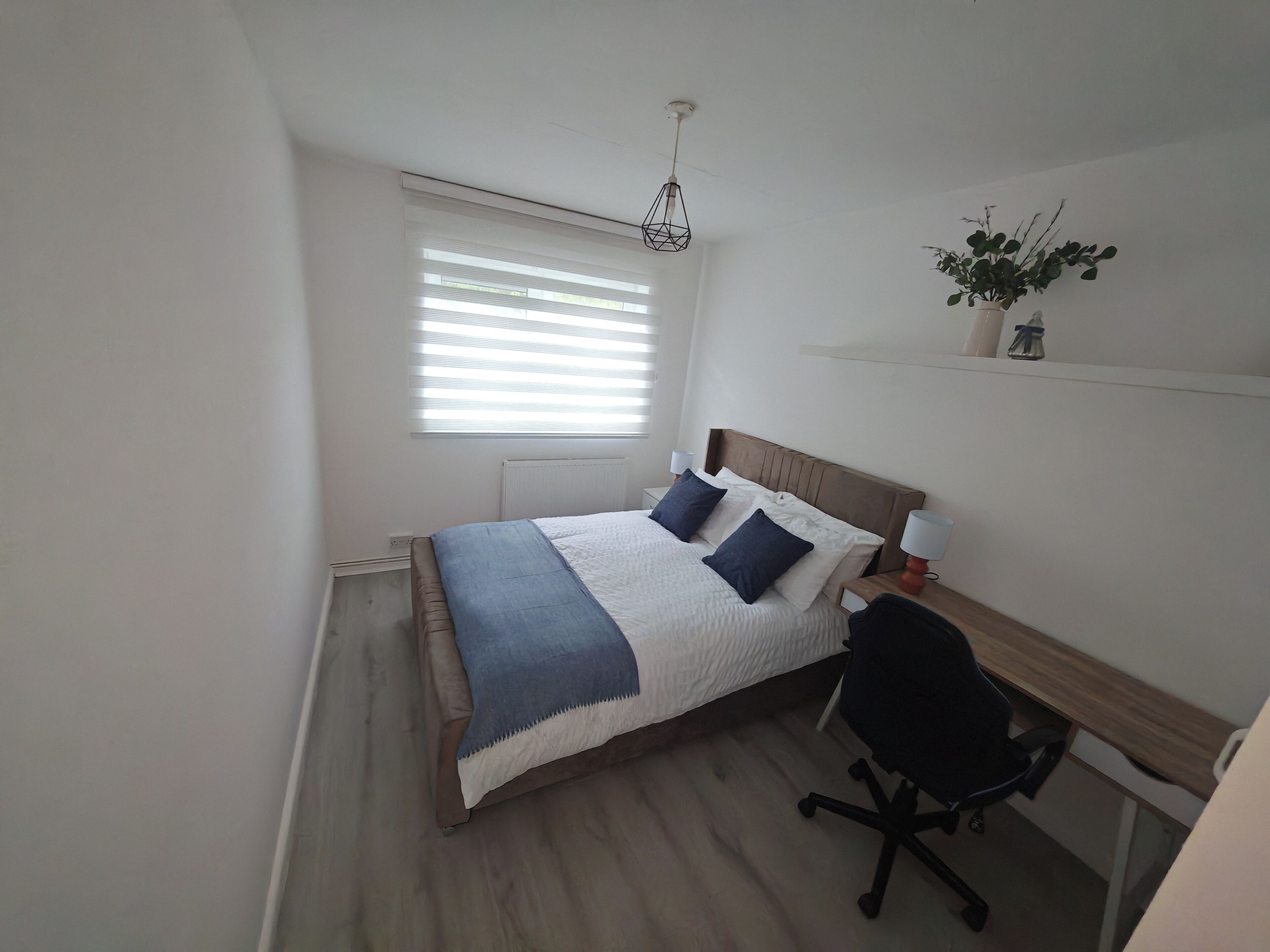 Een slaapkamer met een bed, nachtlampjes, een bureau en een stoel.