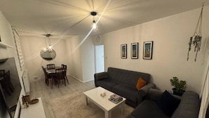 A modern living room with a grey sofa, a coffee table, and a dining area with chairs and a table. - Cosy City Apartment in Central London (London)