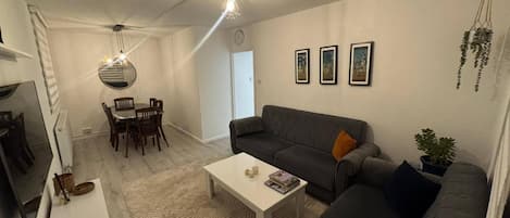 A modern living room with a grey sofa, a coffee table, and a dining area with chairs and a table.