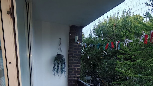 A balcony with a table and chairs, a hanging plant, and a view of trees and clothes drying. - Cosy City Apartment in Central London (London)