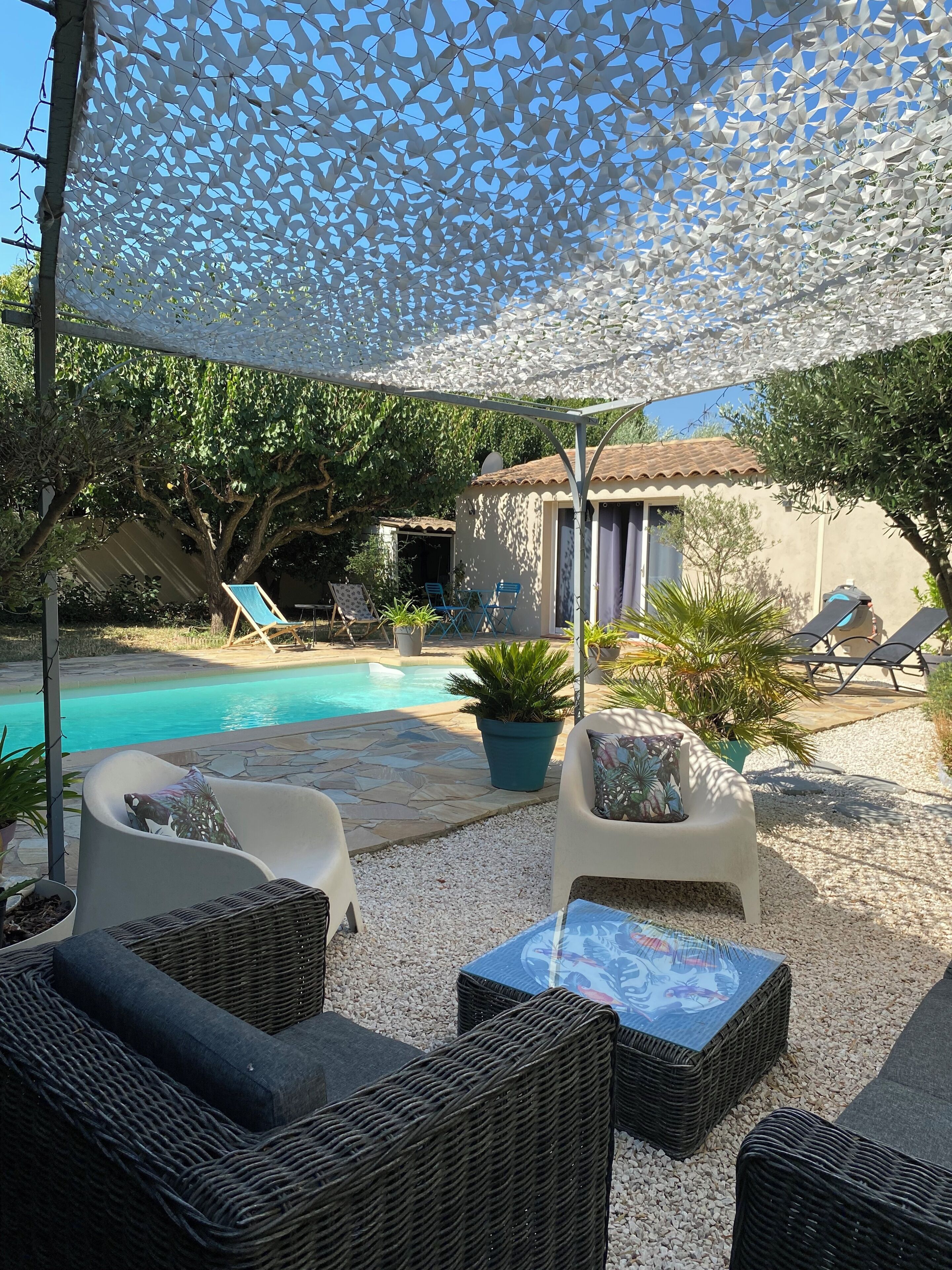 Area salotto esterna con mobili in vimini, piscina e pergolato ombreggiato.