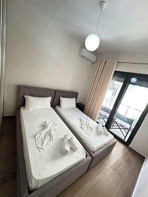 Ein Hotelzimmer mit zwei Betten, einem Deckenventilator, einer Klimaanlage, einem Fenster mit Vorhängen und Blick nach draußen.