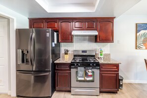 A kitchen with a stainless steel refrigerator, a gas stove, wooden cabinets, and a tiled backsplash.