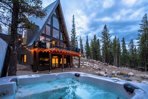 A modern cabin with a hot tub, surrounded by trees.
