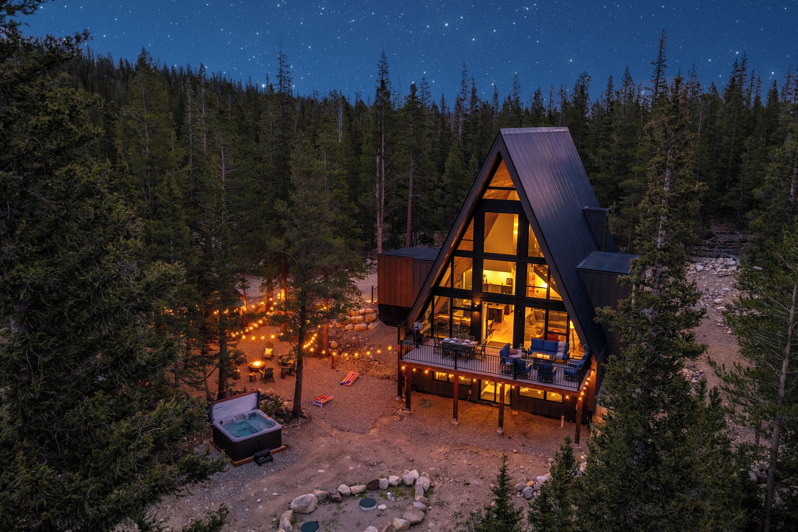 A cabin with a deck, surrounded by trees, and a starry night sky.