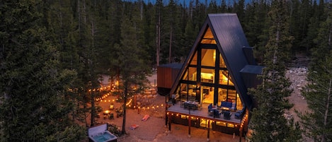 A cabin with a deck, surrounded by trees, and a starry night sky.