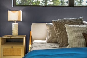 A bedroom with a bed, pillows, a nightstand with a lamp, and a window.