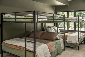 A bunk bed room with green bedding and a window providing a view of trees.