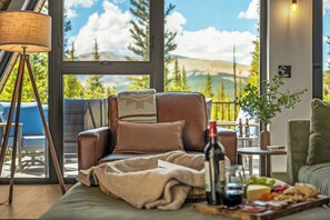 Una sala de estar moderna con un sillón de cuero, una mesita baja con una botella y aperitivos, y vistas al exterior a través de amplios ventanales.