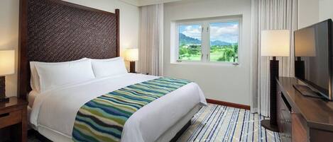 Una habitación de hotel con cama, televisión, ventana con vistas, ventilador de techo y mesita de noche.