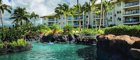 Un resort con piscina cristalina, palmeras y un edificio con balcones.