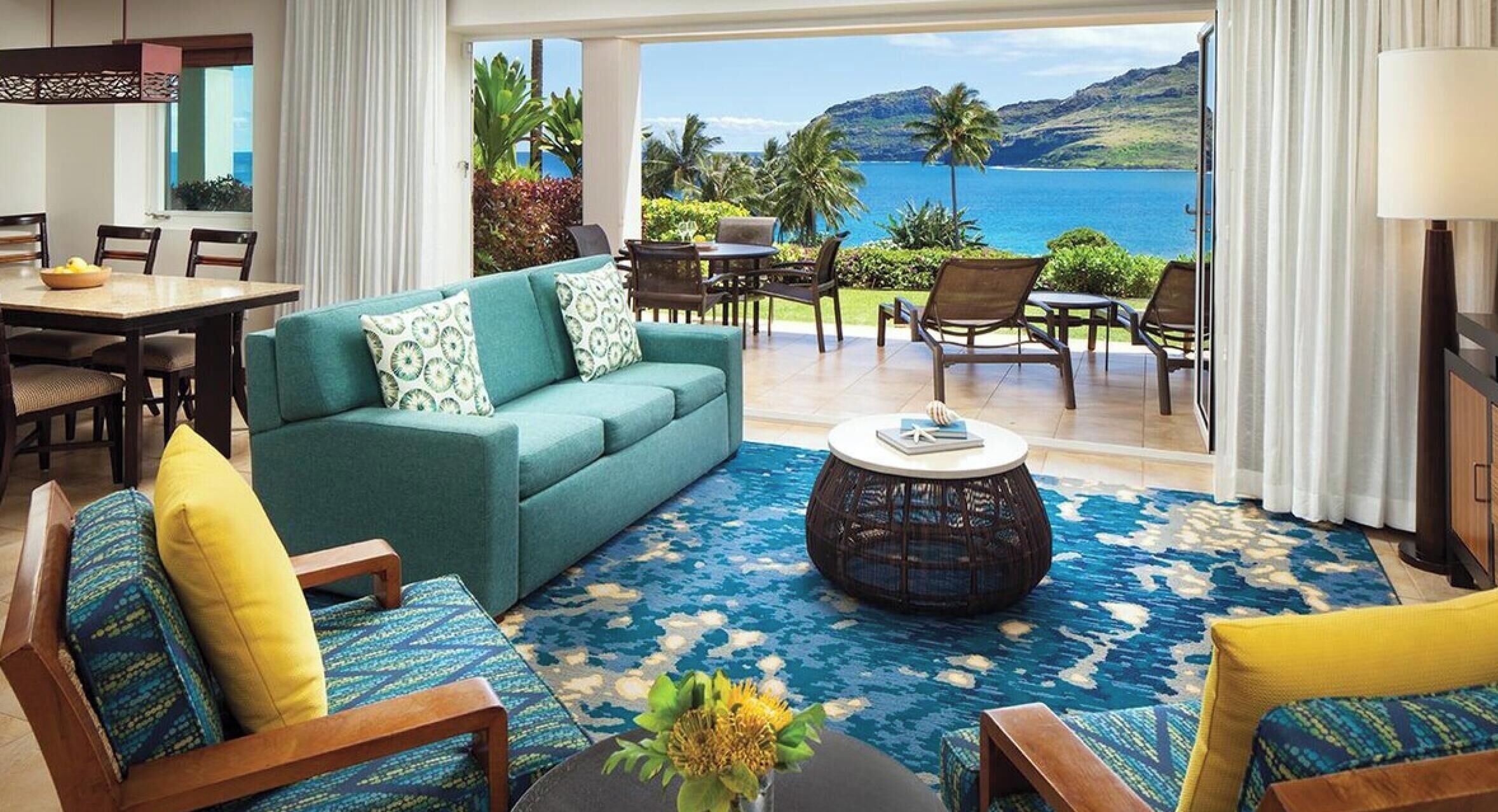 A room with a sofa, chairs, a dining table, and a view of the ocean.