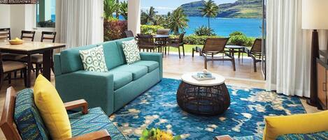 A room with a sofa, chairs, a dining table, and a view of the ocean.