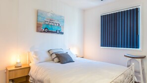 Un dormitorio con cama, una mesita de noche con lámpara, una ventana con persianas y un cuadro colgado en la pared de una furgoneta.