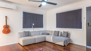 Una habitación con un sofá seccional gris, un ventilador de techo y una guitarra.