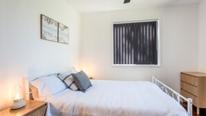 A bedroom with a bed, bedside table, lamp, window with curtains, and a wooden cabinet.