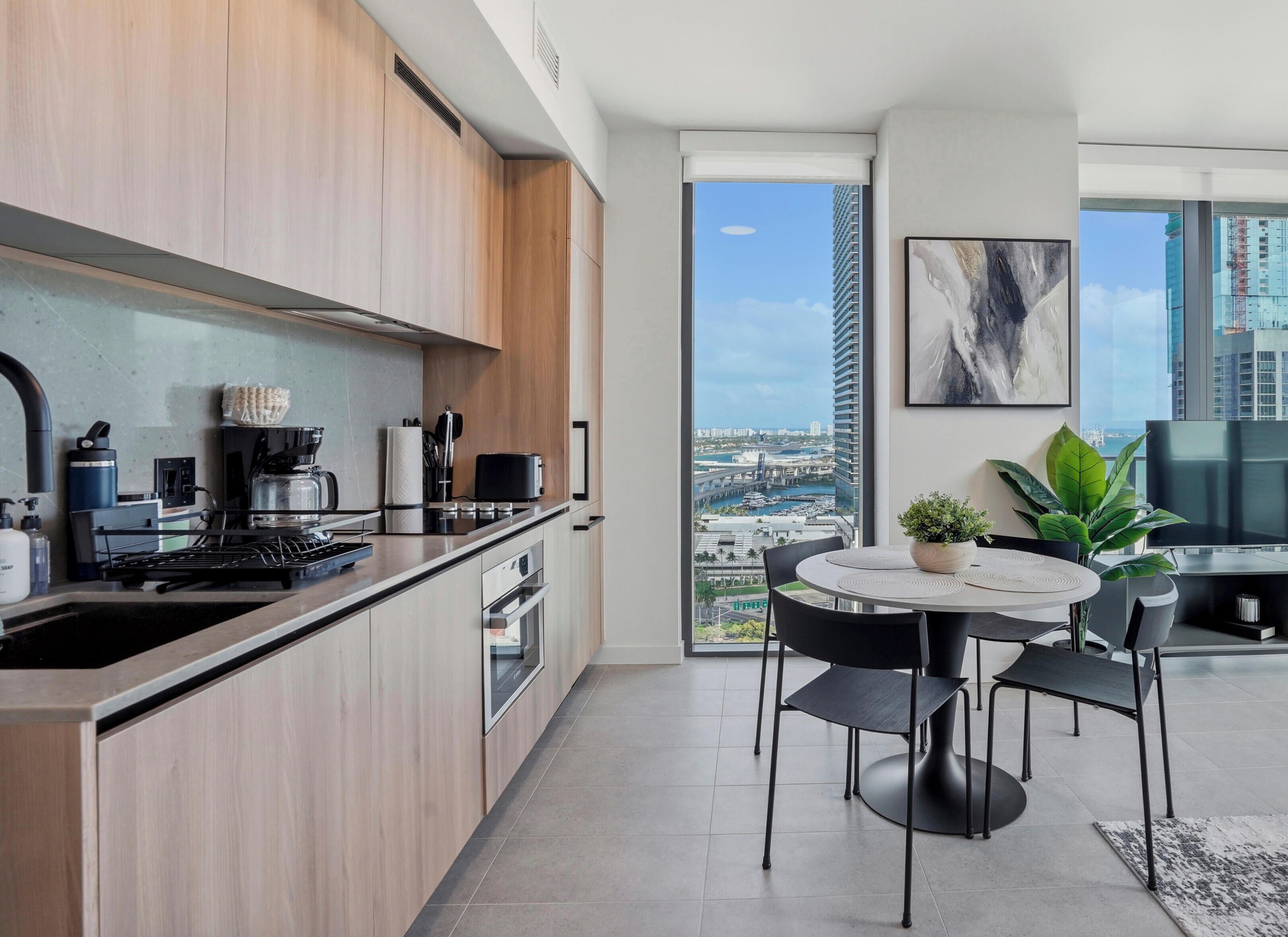 A modern kitchen with a view of a cityscape, a dining area with a round table, and a large window.