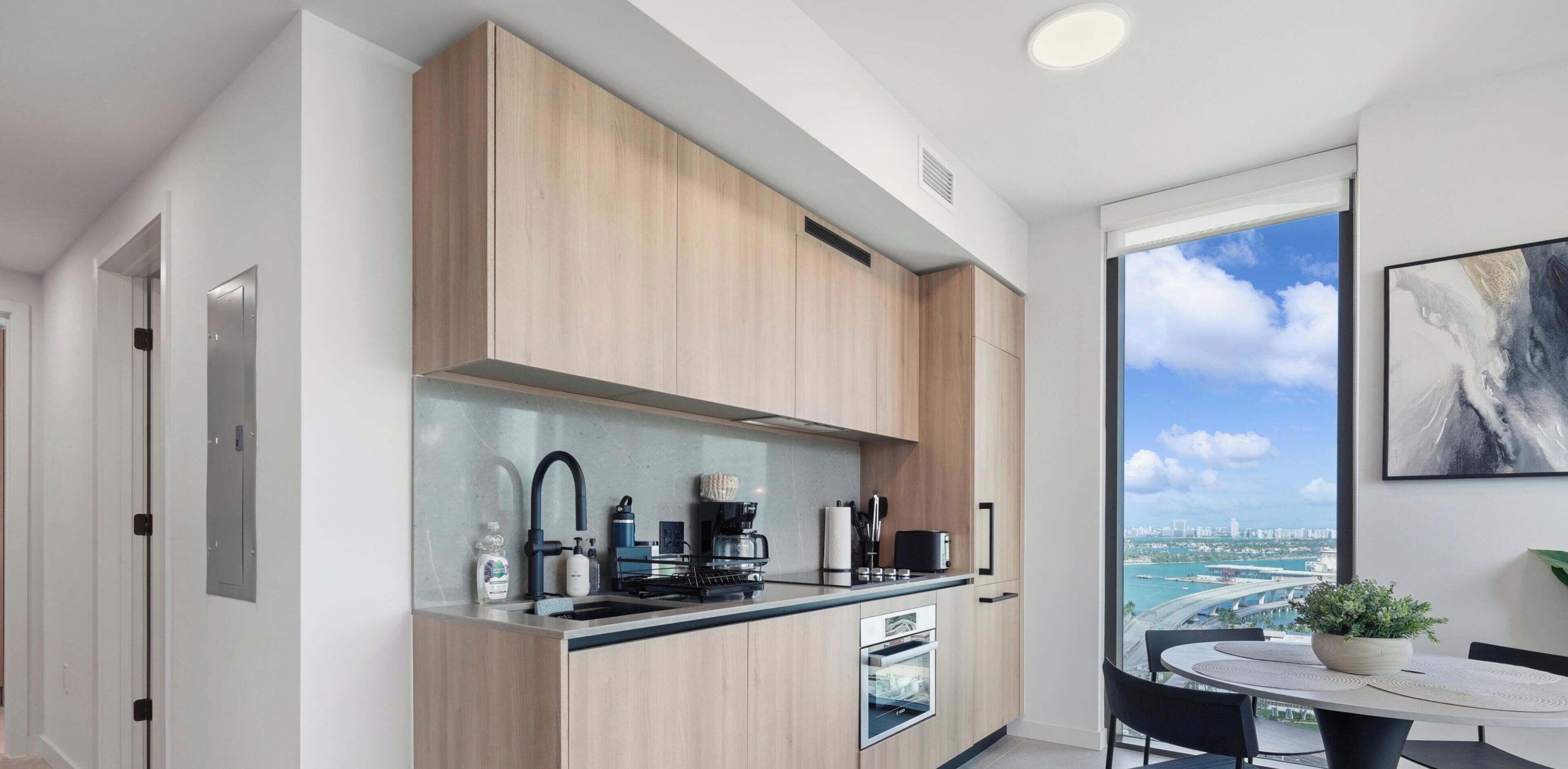 Een moderne keuken met een inbouwoven, een koffieapparaat en uitzicht op een stadsbeeld door een groot raam.