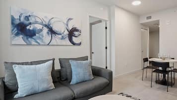 Uma sala de estar moderna com um sofá cinzento, duas almofadas listradas, uma mesa de centro redonda e um quadro na parede.