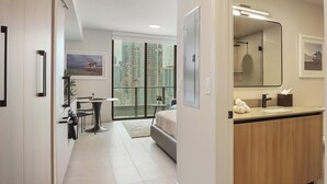 Ein modernes Hotelzimmer mit einem großen Bett, einem Badezimmer mit Spiegel und Waschbecken sowie Blick auf hohe Gebäude.
