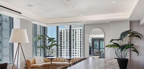 A modern interior with a sofa, a table, and large windows offering a view of high-rise buildings.