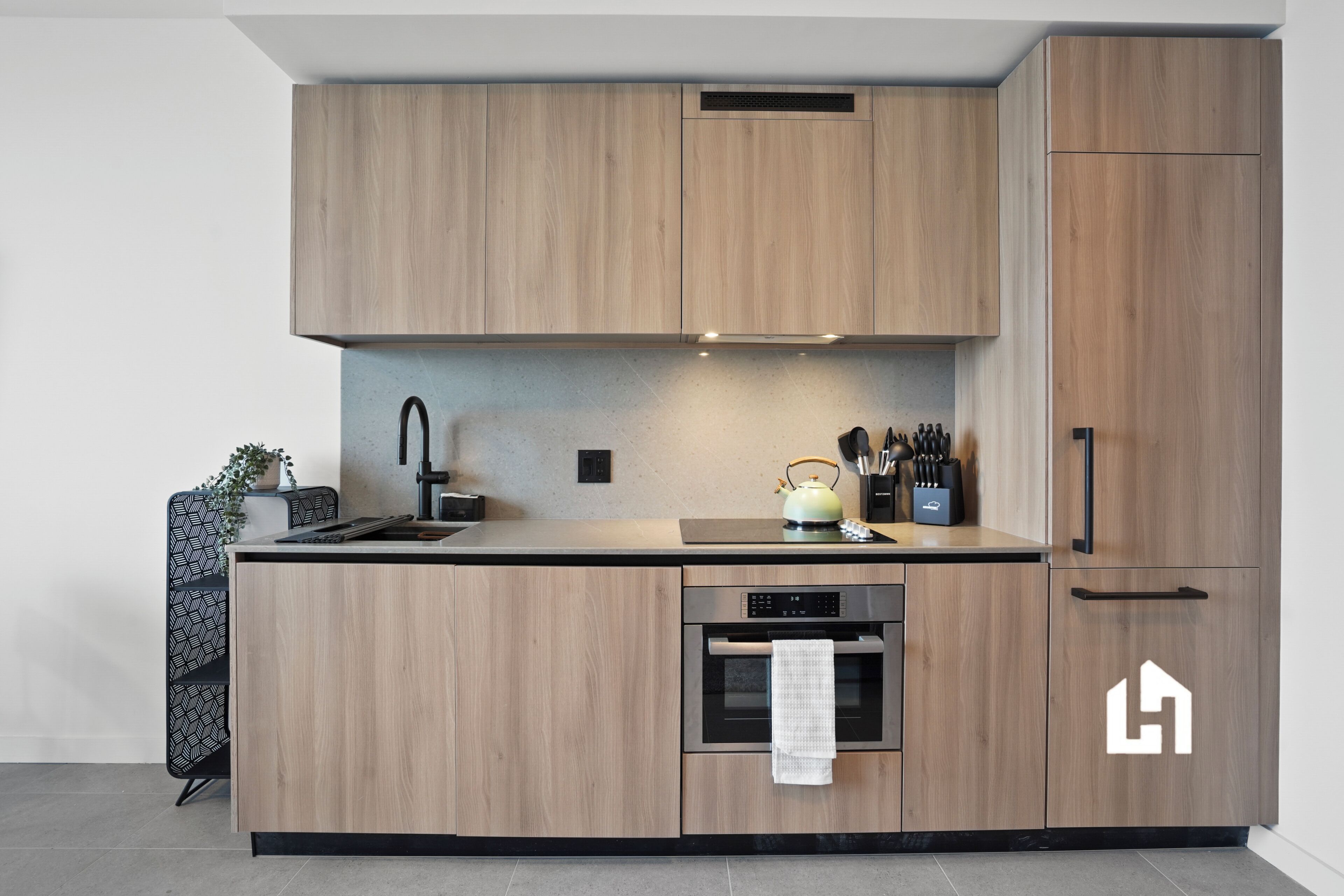 A modern kitchen with wooden cabinets, a built-in oven, and a kettle on the countertop.