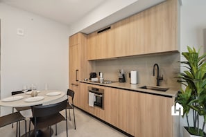A modern kitchen with wooden cabinets, a built-in oven, a sink, and a dining area with a round table and chairs. - 501 First Skyline View Condos (Miami)