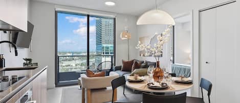 A modern kitchen with a dining area, large windows, and a view of a cityscape.