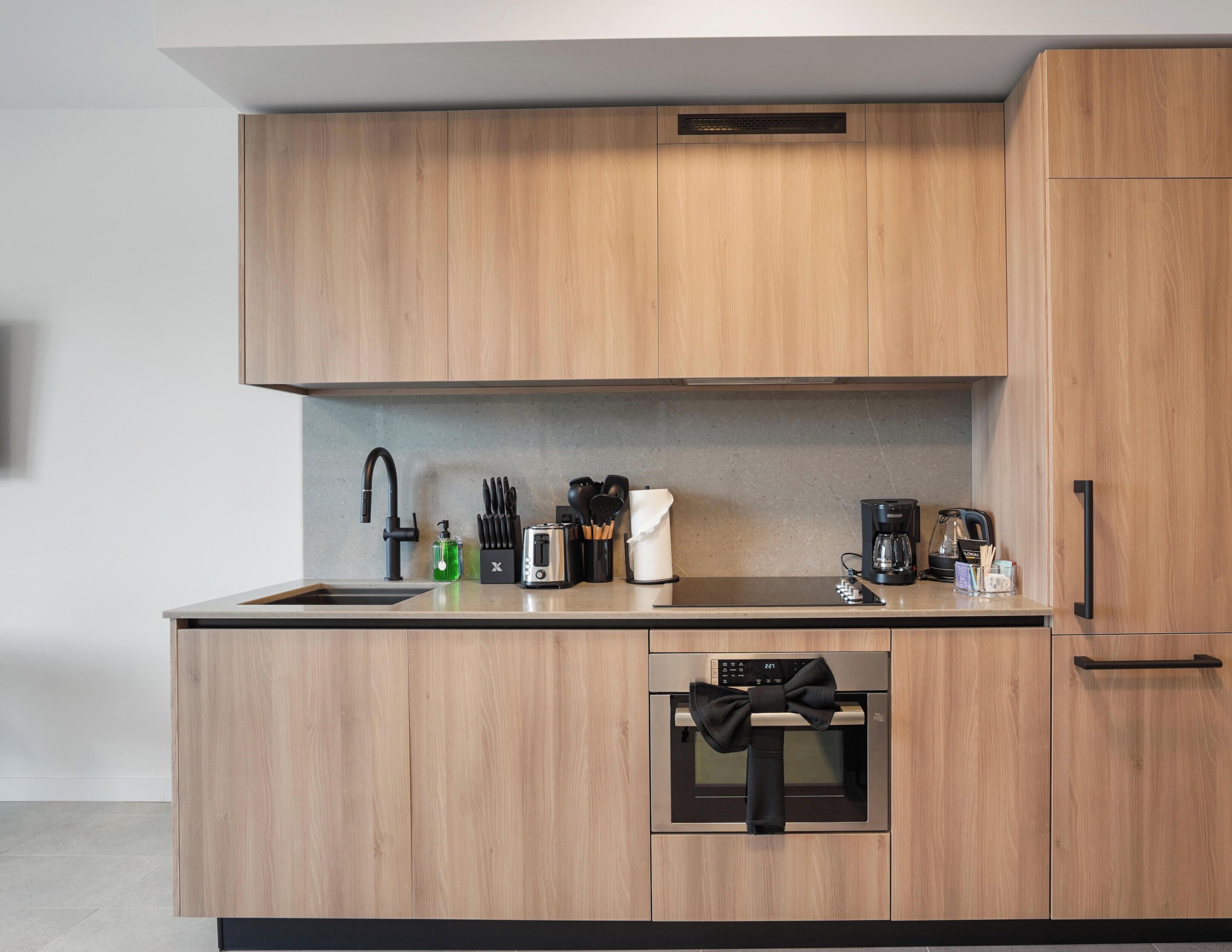 Une cuisine moderne avec des meubles en bois, un four encastré, une machine à café et un grille-pain.