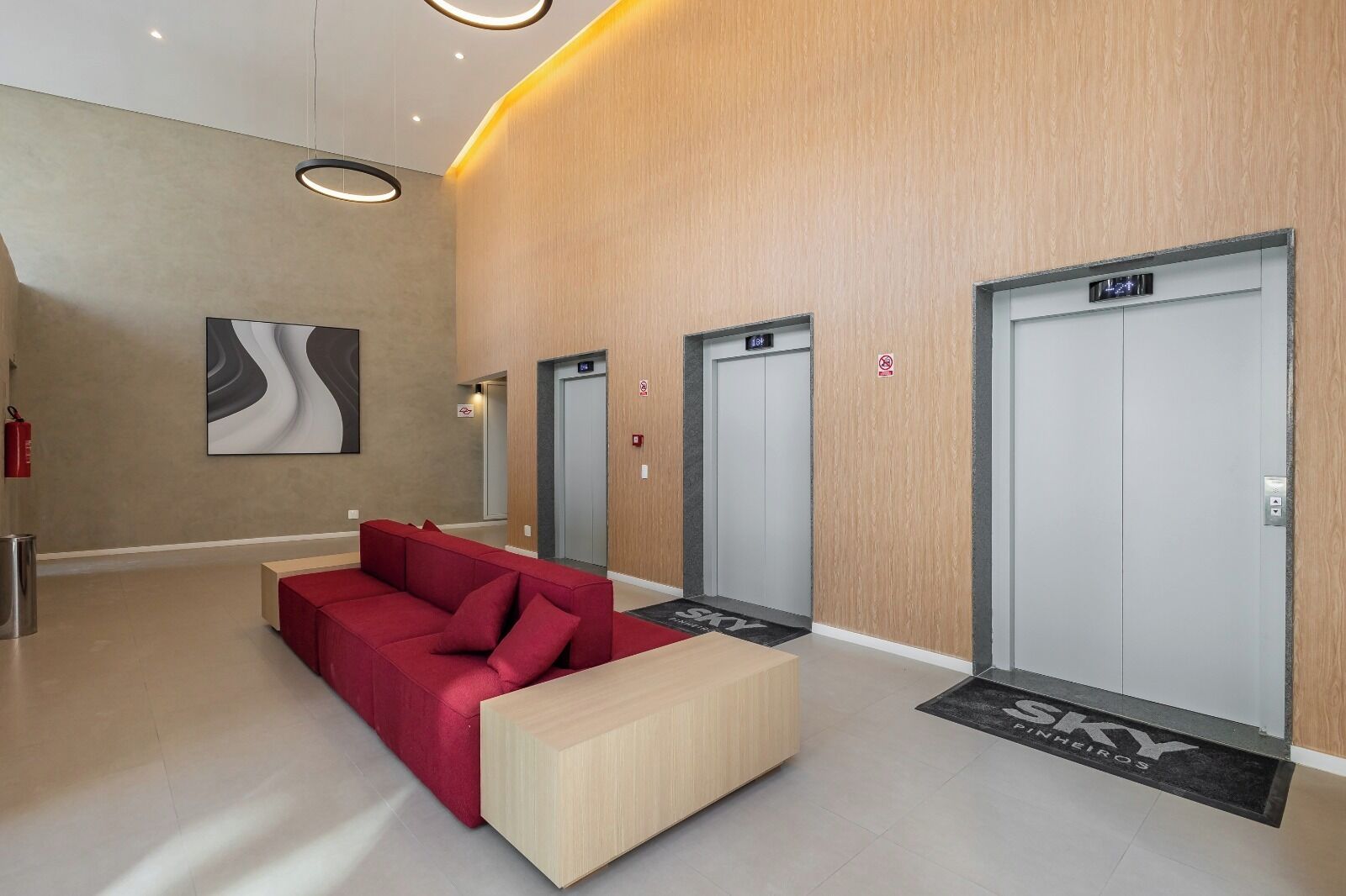A modern lobby with a red sofa, a wooden bench, and three elevators.