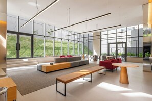 Un vaste salon moderne doté de grandes fenêtres, d’un canapé d’angle, de fauteuils rouges, d’un banc en bois et d’un coin repas.