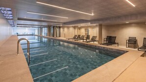 Une piscine intérieure avec un sol carrelé, des chaises longues et une entrée avec une porte en verre.