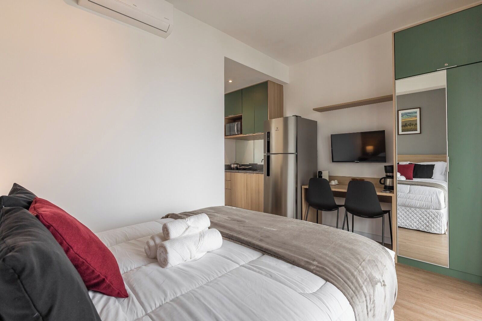 Hotellihuone, jossa on sänky, työpöytä, tuoli, televisio ja pieni keittiönurkkaus.