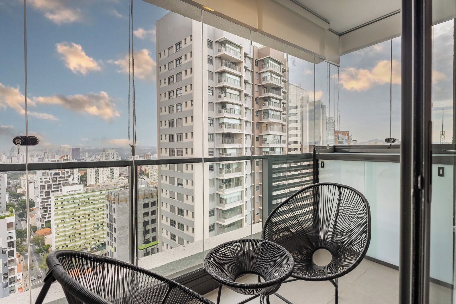 A balcony with two black wicker chairs, a glass railing, and a city view.