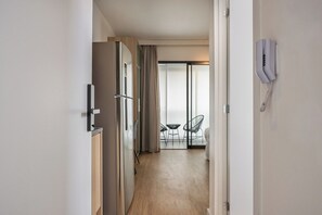 En hotellkorridor med ett modernt kök, en matplats med stolar och en skjutdörr i glas som leder ut till en balkong.