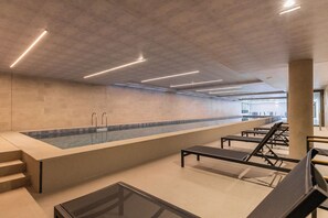 En modern inomhuspool med en lång sittbänkssektion och en glasvägg.