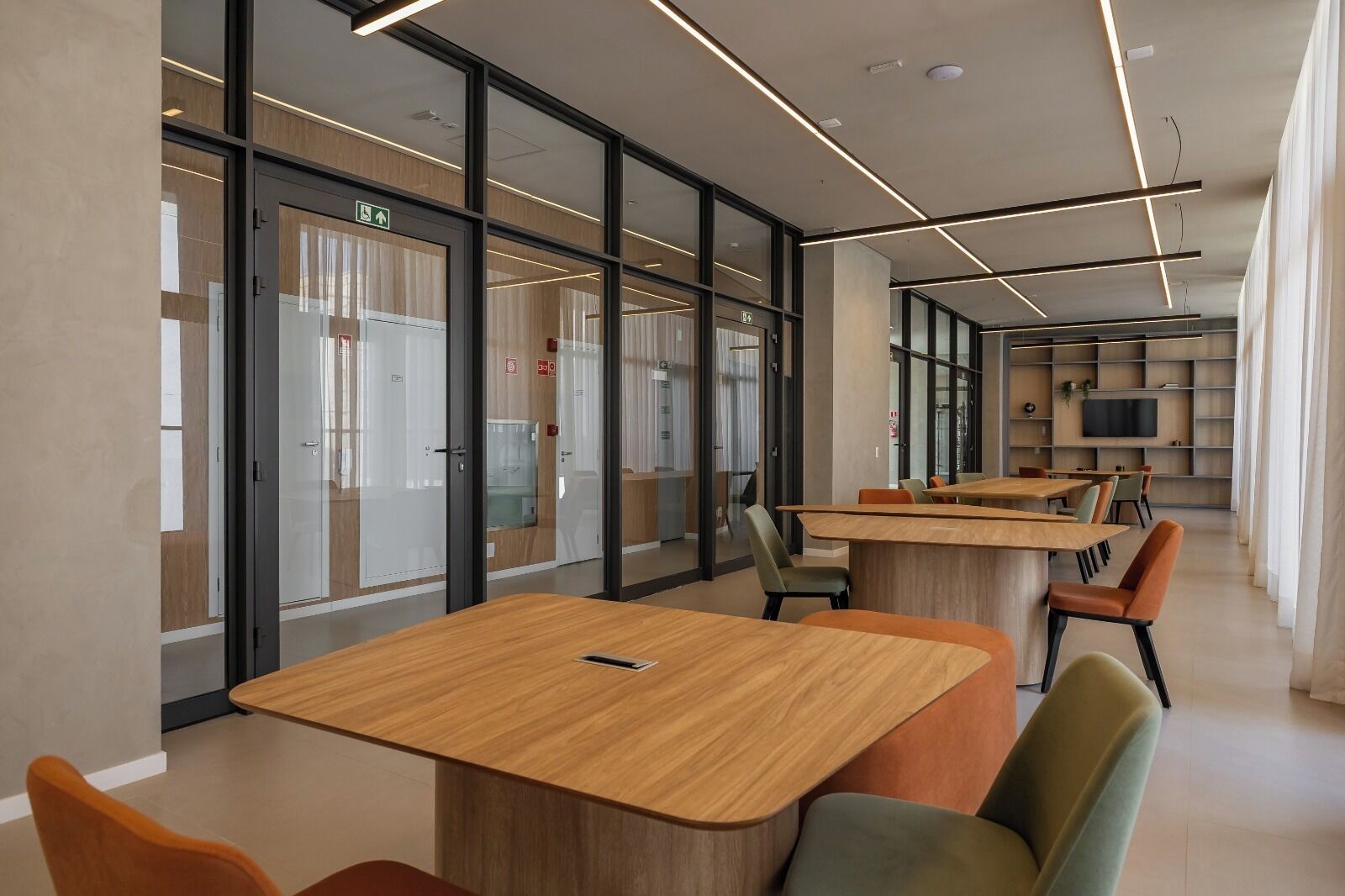 A modern interior with glass partitions, wooden tables, and orange chairs.