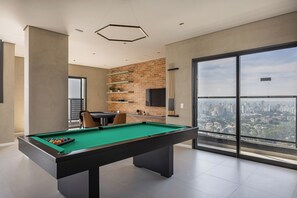 Una mesa de billar moderna en interiores con vista a la ciudad, una pared de acento de ladrillo y un ventanal grande.