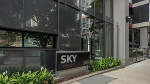 Un immeuble moderne doté d’une grande façade vitrée, d’une enseigne indiquant « SKY Pinheiros 180 Residencial » et d’un petit espace jardin avec des plantes.