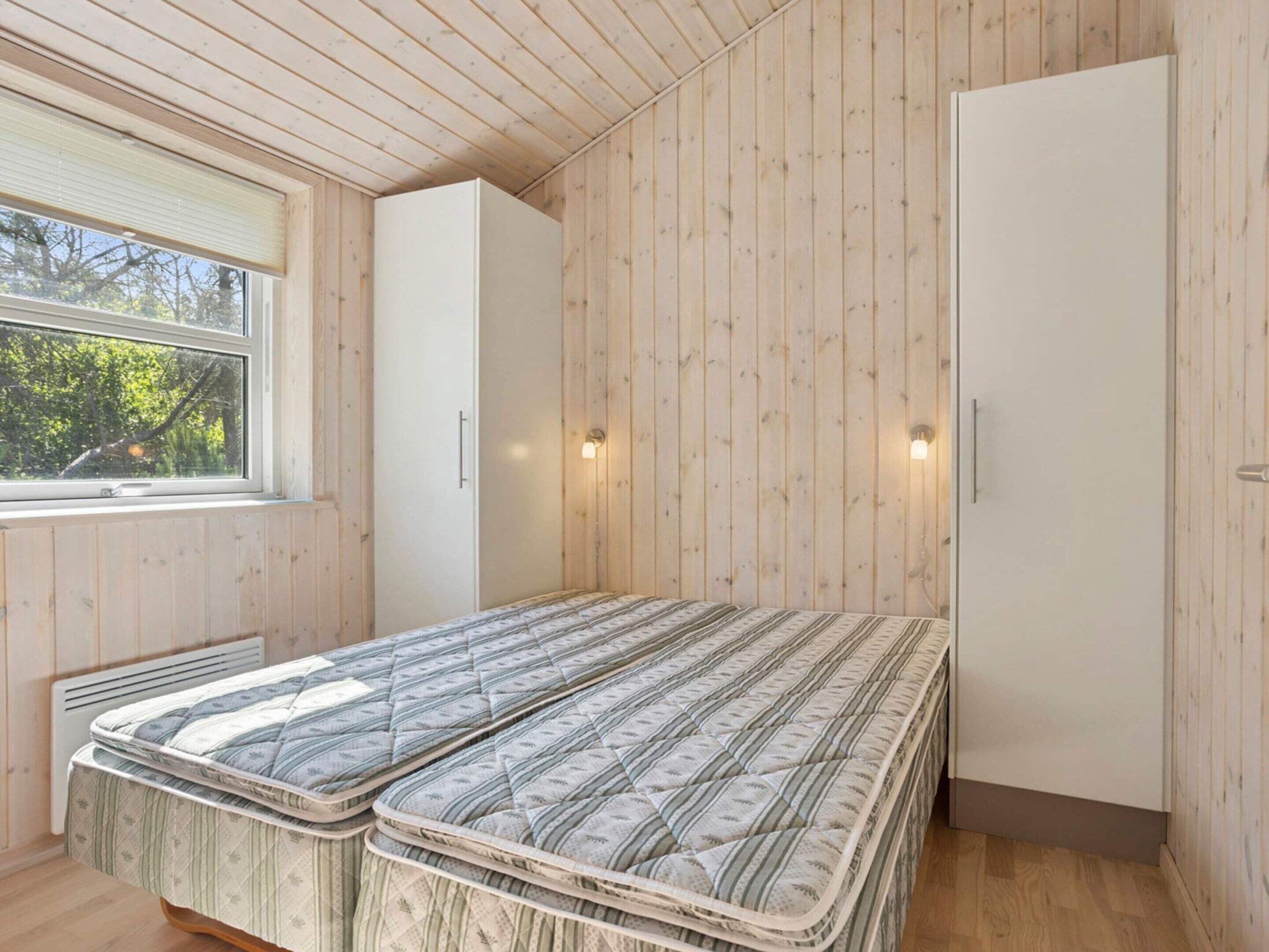 A bedroom with two beds, a window, and wooden walls.
