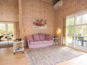 A cozy room with a wooden wall, a purple sofa, a colorful rug, and a large window. - 4 Star Holiday Home in Albaek (Aalbaek)