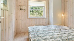 A room with wooden panel walls, a bed with a patterned quilt, a window with a view of trees, and a wall-mounted light fixture. - 4 Star Holiday Home in Albaek (Aalbaek)