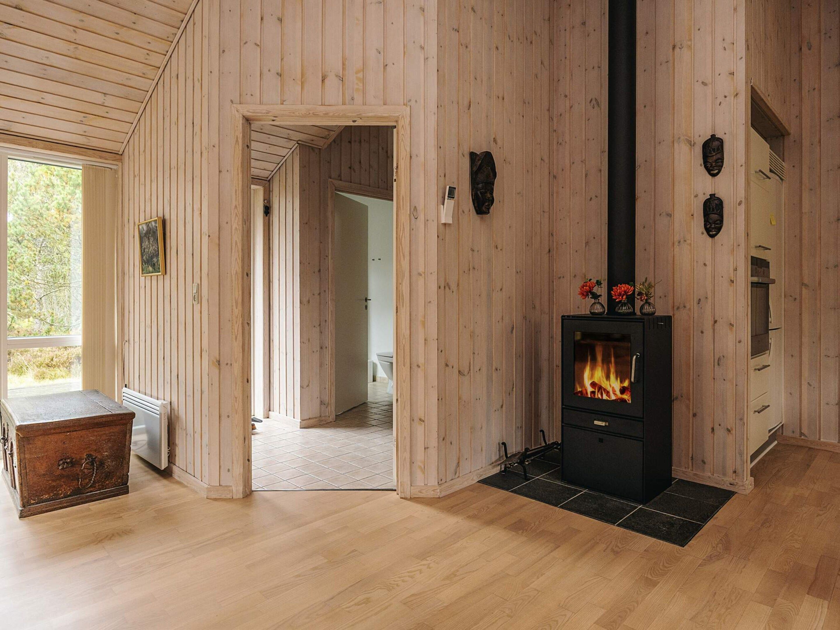 Un interior de madera con chimenea, un cofre de madera y una vista a través de un puerta abierta.