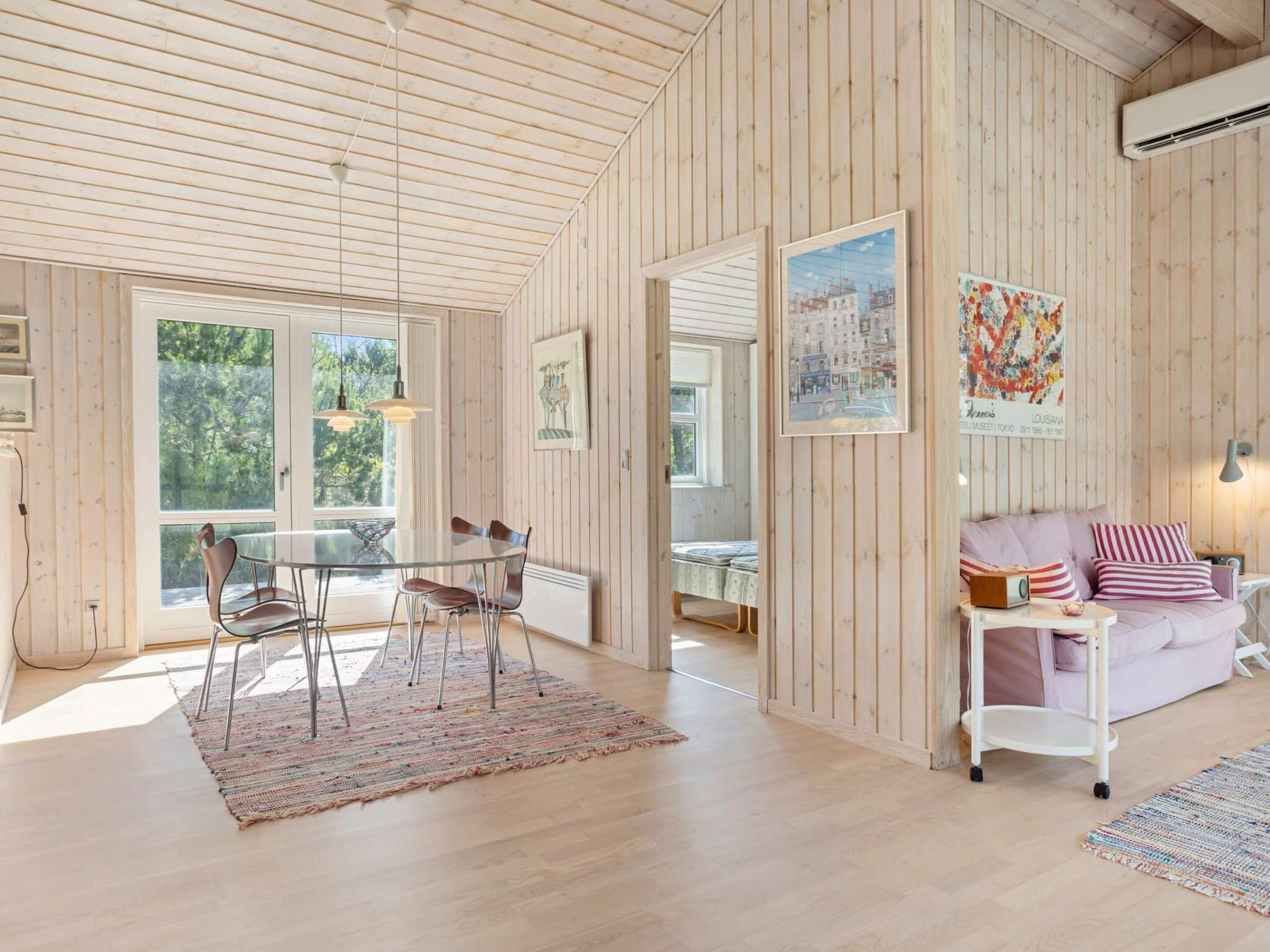 A spacious room with wooden walls, a dining area with a table and chairs, a sofa with cushions, and a painting of a cityscape.