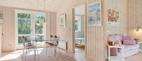 Une pièce spacieuse aux murs en bois, un coin repas avec une table et des chaises, un canapé avec des coussins et un tableau représentant un paysage urbain.