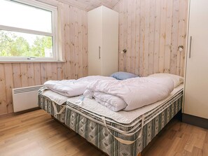 A single bed with a patterned mattress in a room with wooden walls and a window.